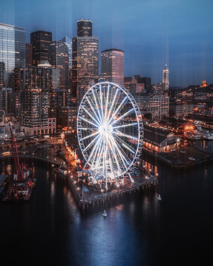 gallery-01 Illuminated Ferris wheel by waterfront with Seattle skyline during twilight, capturing urban vibrance.