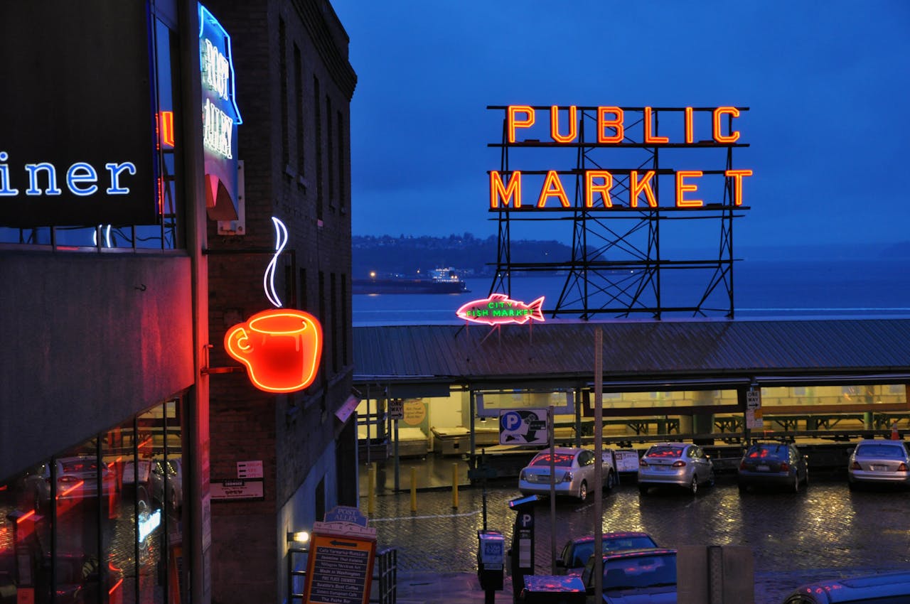 Vibrant nighttime view of Seattle's Public Market with neon coffee and market signs illuminated.